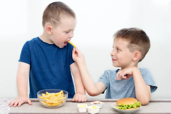 İki mutlu anaokulu çocuğu, fast food için iştahı olan kardeşler. Biri diğerini patates kızartmasıyla besliyor. Yemekler sağlıklı değil, bebek mamasına uygun değil, ama lezzetli, çocuklar mutlu, gülümsüyor.