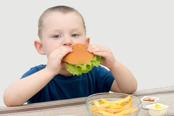 Small Well Fed Boy Sits Table Eats Hamburger Concept Unhealthy — стоковое фото