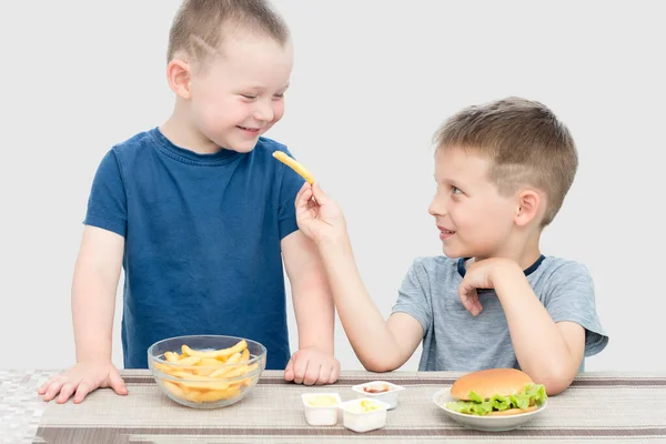 İki tatlı çocuk evde fast food yiyor. Biri diğerine patates kızartması ikram ediyor. Çocuklar mutlu ve gülümsüyor. Konsept sağlıksız, zararlı, yiyecek, ikram, arkadaşlık..