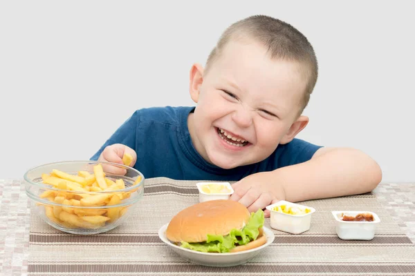 Jongen Zit Vrolijk Aan Tafel Voor Hem Een Hamburger Frietjes — Stockfoto