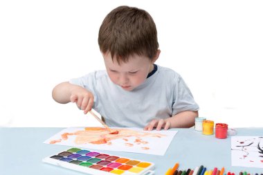 Küçük bir çocuk masaya oturur ve resim çizer. Çocuk nişanlı, çerçeveye bakmıyor. yatay fotoğraf, yumuşak odak