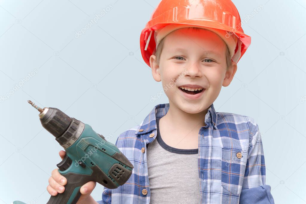 A cheerful,happy child in a construction orange hard hat and holding an electric screwdriver.The concept is that the child plays an adult profession, imitates adults and wants to be like their father.