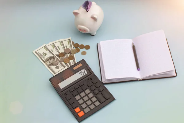 On a blue background, there is a notebook, a calculator, bills, coins and a piggy bank. Horizontal photo artistically processed Idea for planning your monthly expenses Business concept.