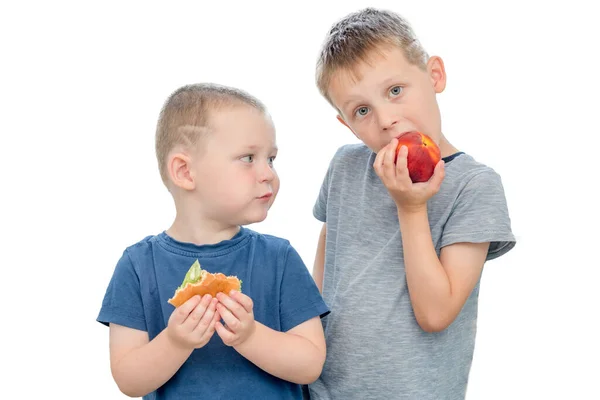 白い背景に2人の男の子が立っています 彼の手にハンバーガーを持つ男の子は 男の子が桃を噛むのを見ています — ストック写真