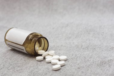 Beyaz tabletler siyah bir cam şişeden gri bir yüzeye döküldü. Kapatmak için. Yatay fotoğrafçılık, yumuşak, seçici odaklanma. Boşluğu kopyala.