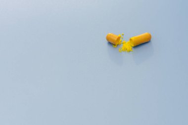 Mavi arka planda sarı hap. Hap, kapsül, ikiye bölündü ve ilaç dışarı döküldü. Minimalizm, yatay fotoğraf