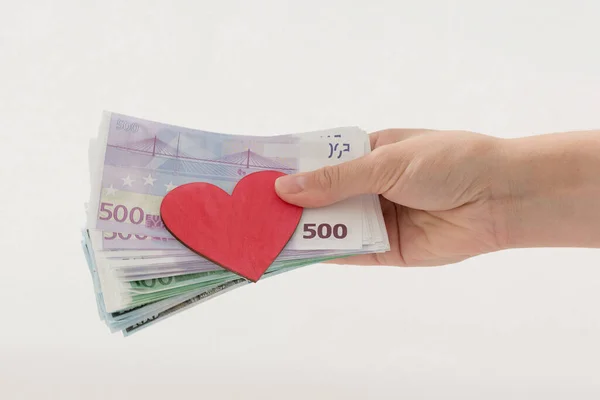 in his hand are Euro notes and a red heart. hand gives money to donate to heart donors CSR concept, health care, organ donation, family insurance world heart day, world health Day