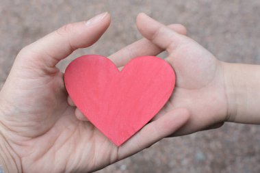 Bir kadın ve bir çocuğun elinde küçük tahta bir kalp. Ana fikir bir annenin çocuğuna olan sonsuz sevgisi, çocukları iyileştirmesi, çocuklara yardım etmesi. Yatay fotoğraf, yakın plan.