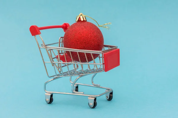 赤いボールのクローズアップはショッピングカートにあります 青の背景 アイデアは 新年のカード 新年の商品の配達 自宅を離れることなくオンラインストアで新年の装飾を購入することです — ストック写真