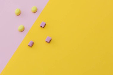 Pastel renklerde fotoğraf, pembe ve sarı şekerler, sarı-pembe arka planda yatar. Üst manzara, yatay fotoğraf. Fikir güzel bir arka plan, metin için bir yer.