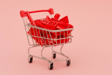 Kırmızı saplı bir alışveriş arabasında. Pembe arka planda inşaatçının kırmızı blokları. Fikir - dünyanın herhangi bir yerinde herhangi bir mal, inşaat, teslimat, çevrimiçi mağaza.