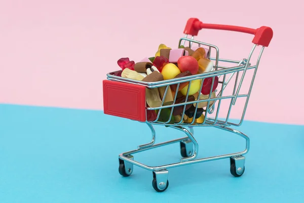 Różowym Niebieskim Tle Wózek Supermarketu Wypełniony Kolorowymi Słodyczami Marmoladą Fotografia — Zdjęcie stockowe