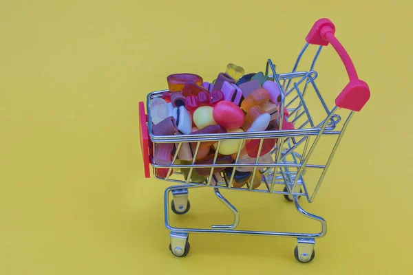 一辆黄色背景的超级市场的小推车 里面装满了五彩缤纷的糖果和果酱 任何产品的送货上门 网上购物 假日准备 — 图库照片