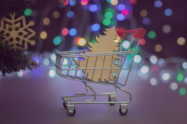 クリスマスライトを背景に木製のクリスマスツリーを持つミニカートのクローズアップ コンセプト 休日の買い物 クリスマスの販売 クリスマスの準備 新年に近づく — ストック写真