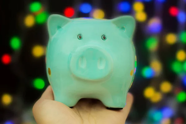 A piggy bank in the form of a pig stands on his hand, against the background of New Year\'s lights. Concept - saving money, saving, end of the year - summing up, planning for the next year.