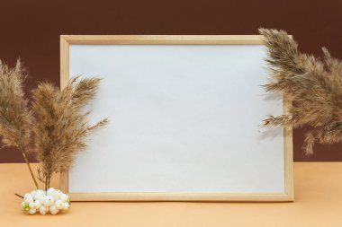 Kahverengi arka plandaki model çerçeveler, kurumuş çiçeklerin kabarık dalları ve beyaz böğürtlenler. Sonbahar hala hayattır. Geçmişi. Kavram - sonbahar fotoğraf çerçevesi, metin yeri, fotokopi makinesi.