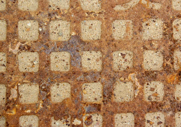 Rusty sewer manhole cover. Geometric pattern on the cover of the sewer manhole. The dents in the sewer manhole are covered with sand. Close-up view of the texture of the old rusty sewer manhole.