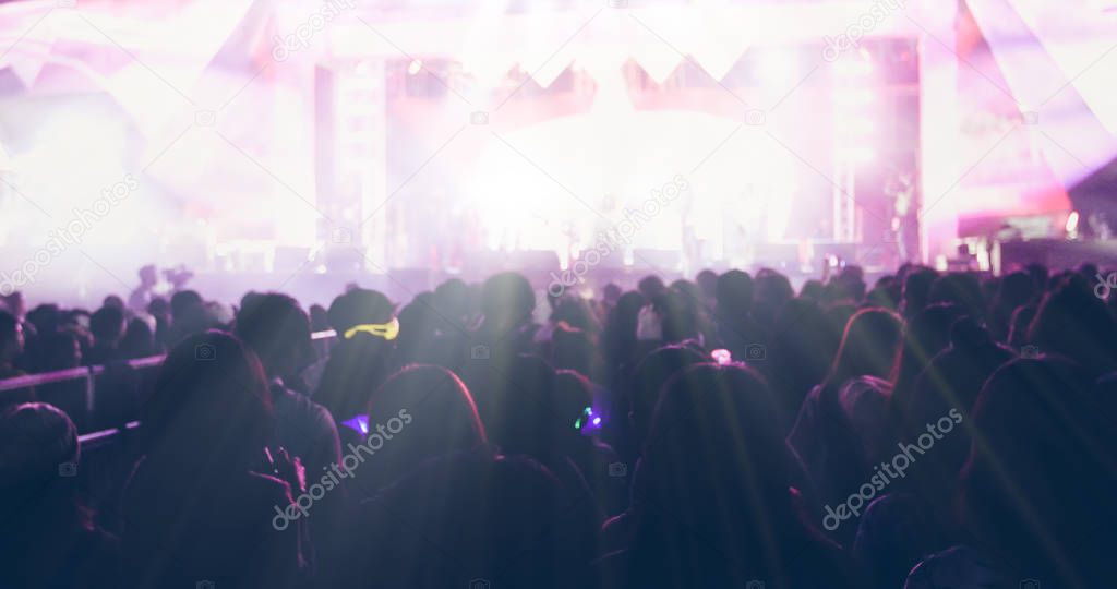 blurry of silhouettes of concert crowd at Rear view of festival crowd raising their hands on bright stage lights