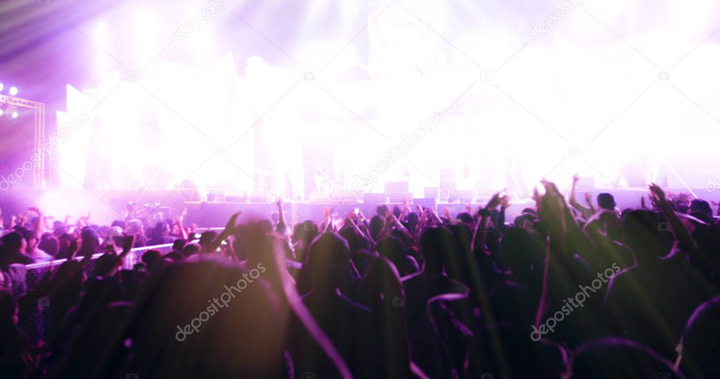 blurry of silhouettes of concert crowd at Rear view of festival crowd raising their hands on bright stage lights