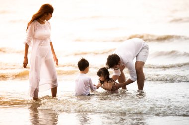 Aktif ebeveynler ve insanlar yaz tatillerinde ve çocuklarla tatilde açık hava aktiviteleri. Mutlu aile ve oğul kumsalda gün batımı denizinde eğlenceli bir şekilde yürürler.. 