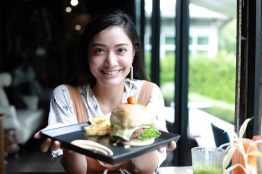 Asyalı kadınlar gülümsüyor, mutlu ve dinlenirken kahve ve restoranda hamburger yemekten zevk alıyorlar.