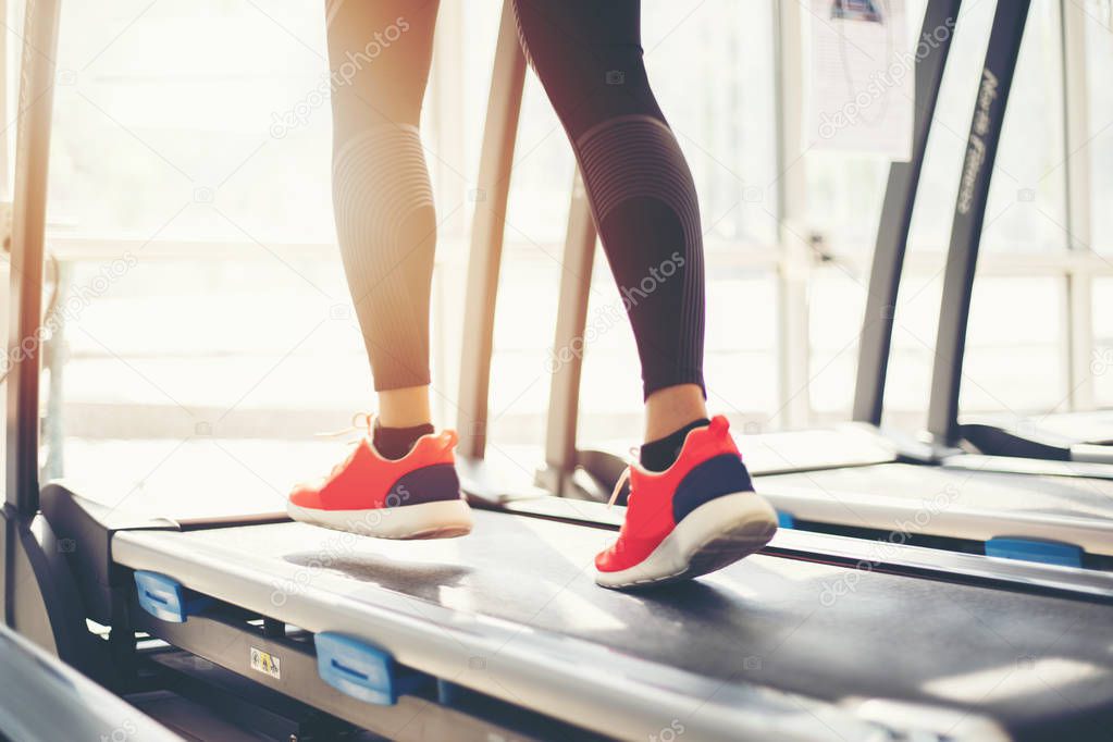 Blurry of  running sport shoes at the gym while a young caucasian woman is having jogging on the treadmill