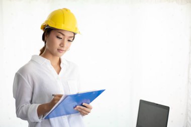 Asyalı kadın mühendisler denetliyor, çalışıyor ve ofiste planları tutuyor.