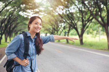 Araba bekleyen Asyalı kadın turistler ve gezginler ve yol kenarında kollarını açmış duran Özgürlük yolcusu kadın..
