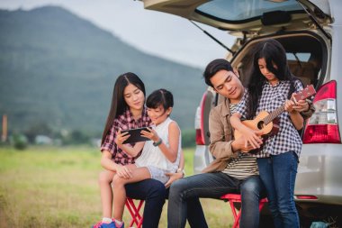 Asya aile t oturmuş ukulele oynamaktan mutlu küçük kız