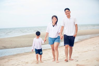 Aktif ebeveynler ve insanlar yaz tatillerinde ve çocuklarla tatilde açık hava aktiviteleri. Mutlu aile ve oğul kumsalda gün batımı denizinde eğlenceli bir şekilde yürürler.. 