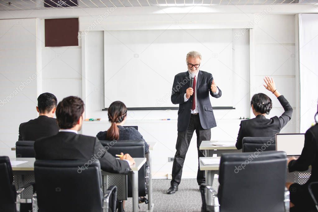 Business Audience raising hand up while businessman is speaking in training for Opinion with Meeting Leader in Conference Room