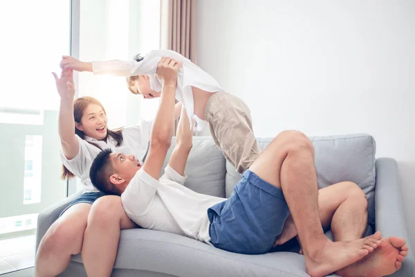 Happy asian family with son playing and laughing on sofa at home