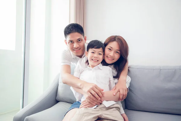 Happy asian family with son laughing and embracing on sofa at home