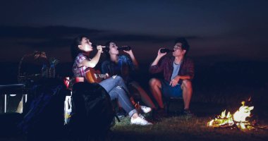 Mutlu genç Asyalı arkadaşlar turist grubu içme ve göl yakınında kamp birlikte gitar çalmak 