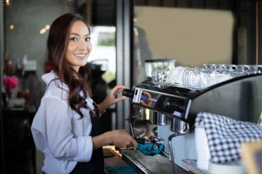 Asyalı kadın barista gülümseyen ve kahve dükkanı tezgahında kahve makinesi kullanarak. Küçük işletme sahibi kavramı.