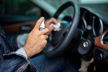 Koronavirüs koruması için arabayı temizlemek için sprey alkol kullanan Asyalı bir adam.