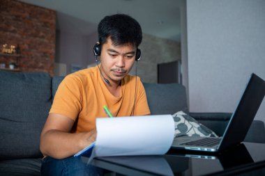 Asyalı işadamları defter bilgisayarları kullanıyor ve online toplantılarda kulaklık takıyor ve evden çalışıyorlar..