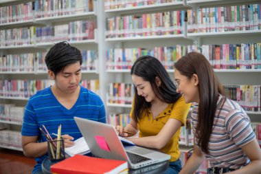 Grup Asyalı Öğrenciler Gülümseyin ve kitap okuyun ve defter kullanarak iş ve proje fikirlerini paylaşın