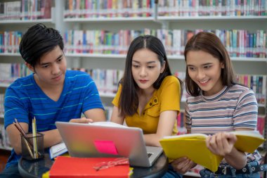 Grup Asyalı Öğrenciler Gülümseyin ve kitap okuyun ve defter kullanarak iş ve proje fikirlerini paylaşın