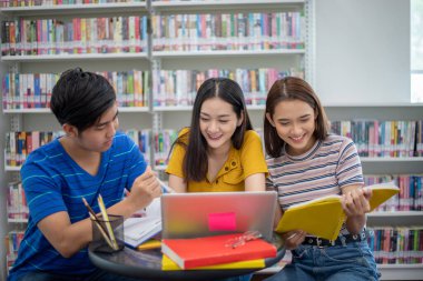 Grup Asyalı Öğrenciler Gülümseyin ve kitap okuyun ve defter kullanarak iş ve proje fikirlerini paylaşın