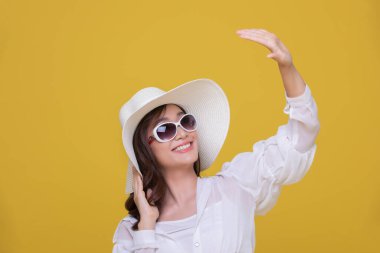 Asyalı güzel, mutlu, güneş gözlüklü, şapkalı, neşeli bir genç kız portresi. Ve sarı stüdyo arka planında izole edilmiş kameraya bakıyor..