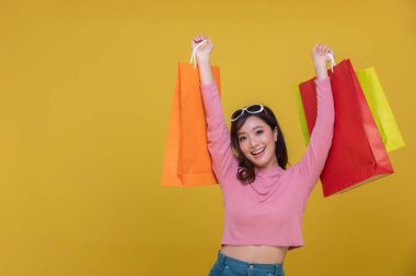 Asyalı güzel, mutlu, neşeli bir genç kadın portresi sarı arka planda izole edilmiş alışveriş çantaları taşıyor. Mutluluk, tüketim, satış ve alışveriş danışmanları.
