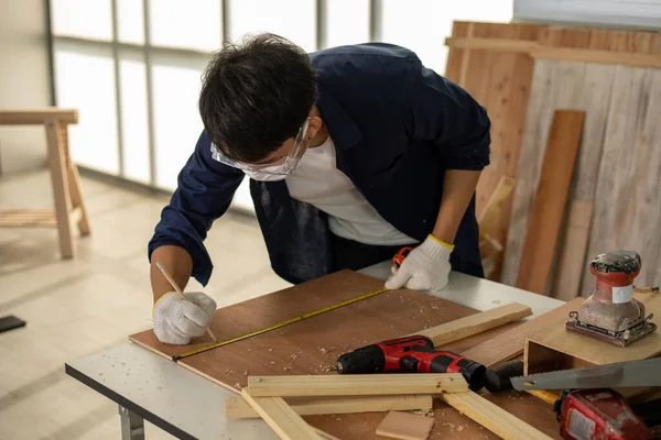 Asian man Carpenter working with technical drawing or blueprint construction paper lying on a workshop with carpentry tools and wood at home