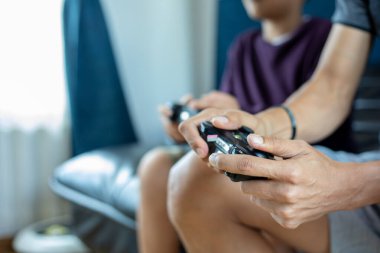 Asyalı baba ve oğul video oyunlarının keyfini çıkarıyorlar. Oyun çubuğuyla birlikte. Heyecanlı ve eğlenceli bir şekilde evde oturuyorlar.