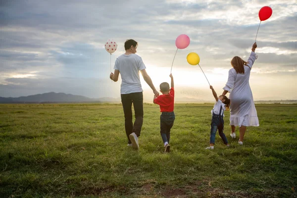 Asian family holding balloon and walking on the Meadow at sunset with happy emotion. Family Holiday and Travel concept.