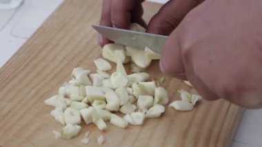 Una mano de un chico cortando dientes de ajo sobre una tabla de madera con un cuchillo. Bir çocuğun eli, tahta bir tahtanın üzerinde bıçakla sarımsak karanfili kesiyor..