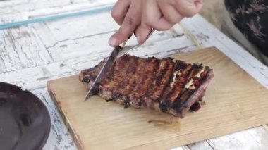 Una mano de un chico con un cuchillo cortando costillas sobre una tabla de mader. ahşap bir tahtada kaburga kesen bir çocuğun eli..