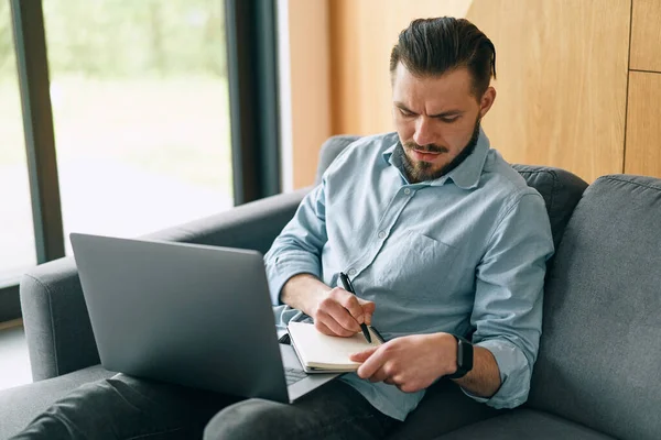 Frustrated brunette man freelancer working with laptop and making notes