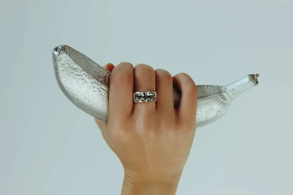 Woman hand with silver ring holding silver banana