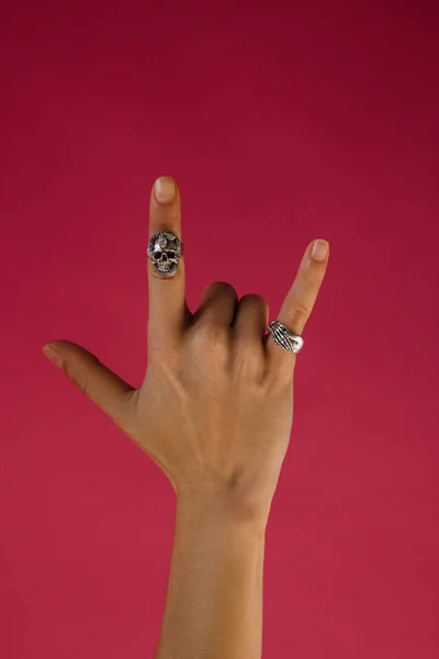 Woman hand with silver rings making rock sign on pink background